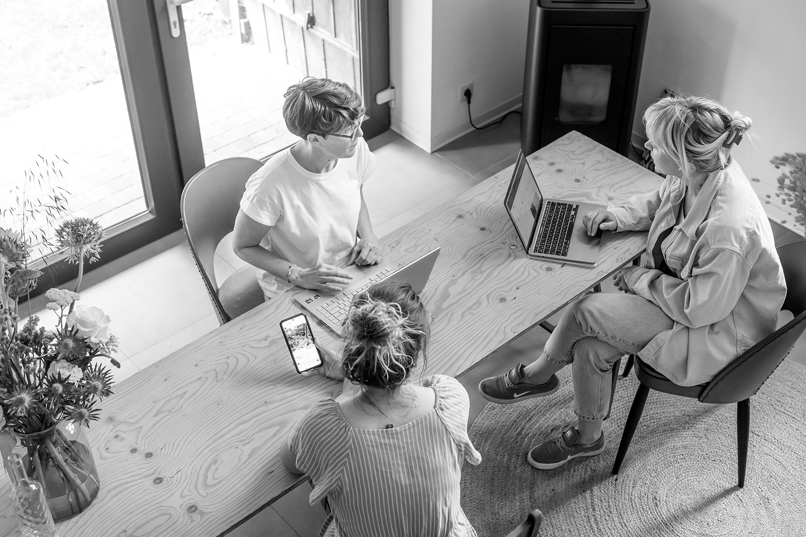 Drie dames rond een tafel die aan het telewerken zijn en iets met elkaar bespreken over social media.